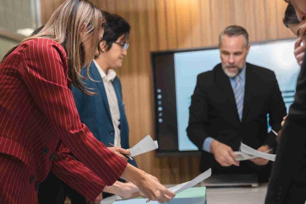 A group of business people discussing documents while standing around a table in a professional setting.
