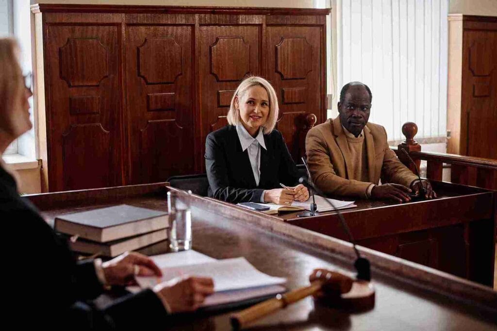 A woman seated at a desk in a courtroom, focused and engaged in the proceedings around her.