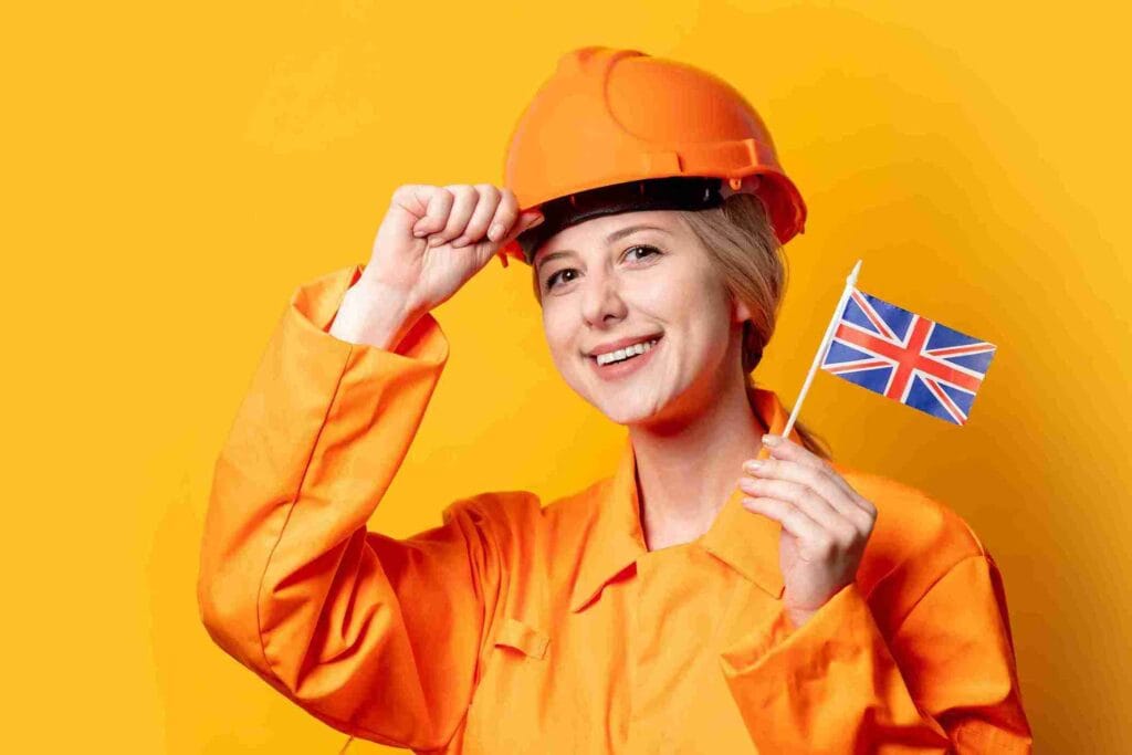 A woman wearing an orange hard hat proudly holds a British flag, smiling against a bright background.