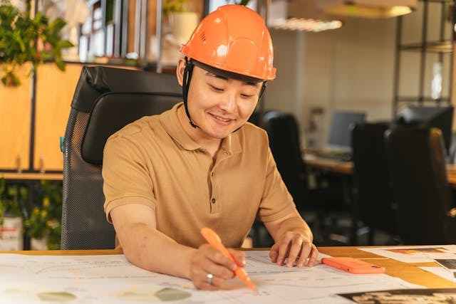 A woman in an orange hard hat holds a piece of paper, looking focused and ready for her task.
