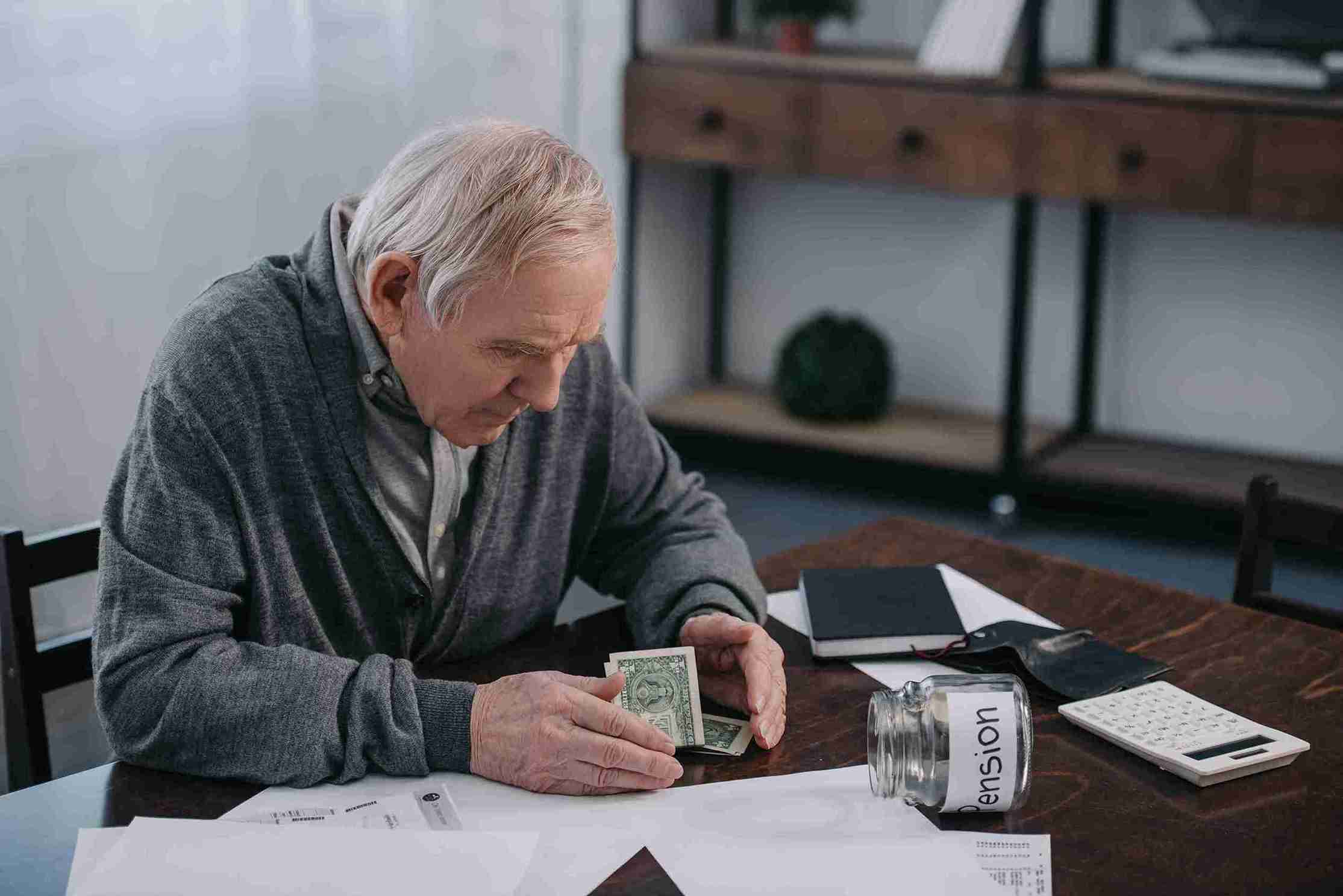 worried senior man counting money at table and wondering how much to make a will