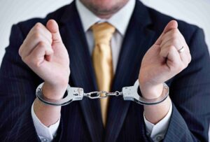 UK White Collar Crime Cases (in the image a man guilty of a white collar crime case can be seen with handcuffs)