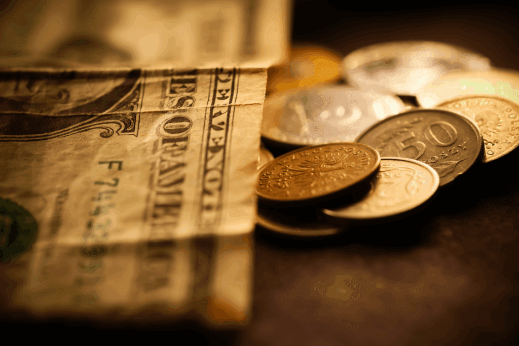 A close-up of a pile of coins stacked beside a crumpled dollar bill on a flat surface.