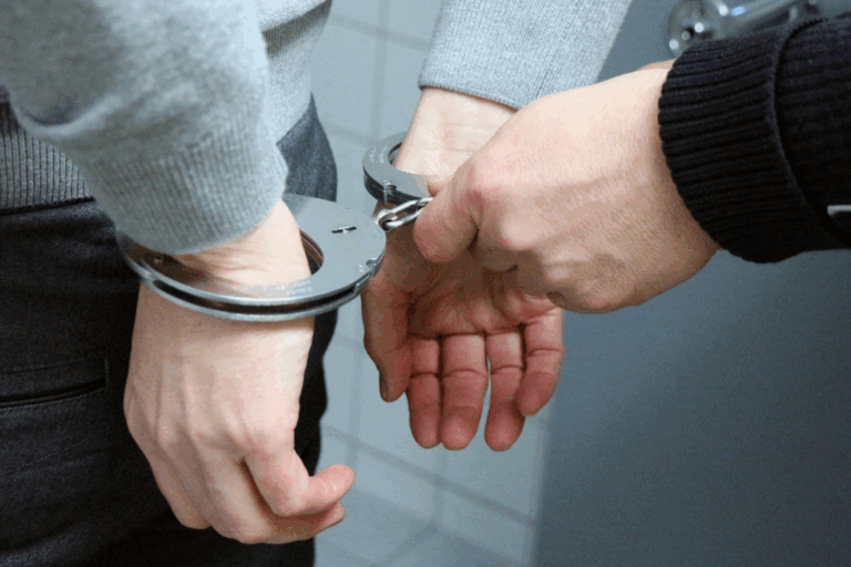 A man holds handcuffs in front of another person, suggesting a tense or confrontational situation.