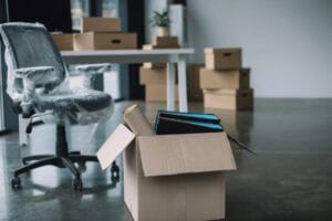 (An office chair wrapped in plastic next to moving boxes, representing the start of a business relocation UK process.)