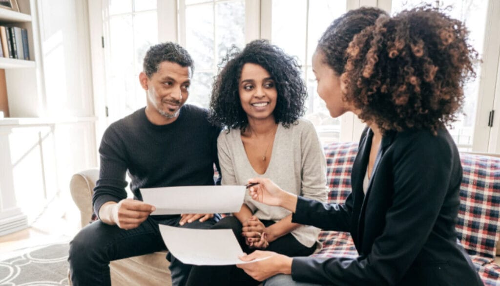 A couple sitting on a sofa, smiling as they review visa application documents with a professional legal consultant in a brightly lit office
