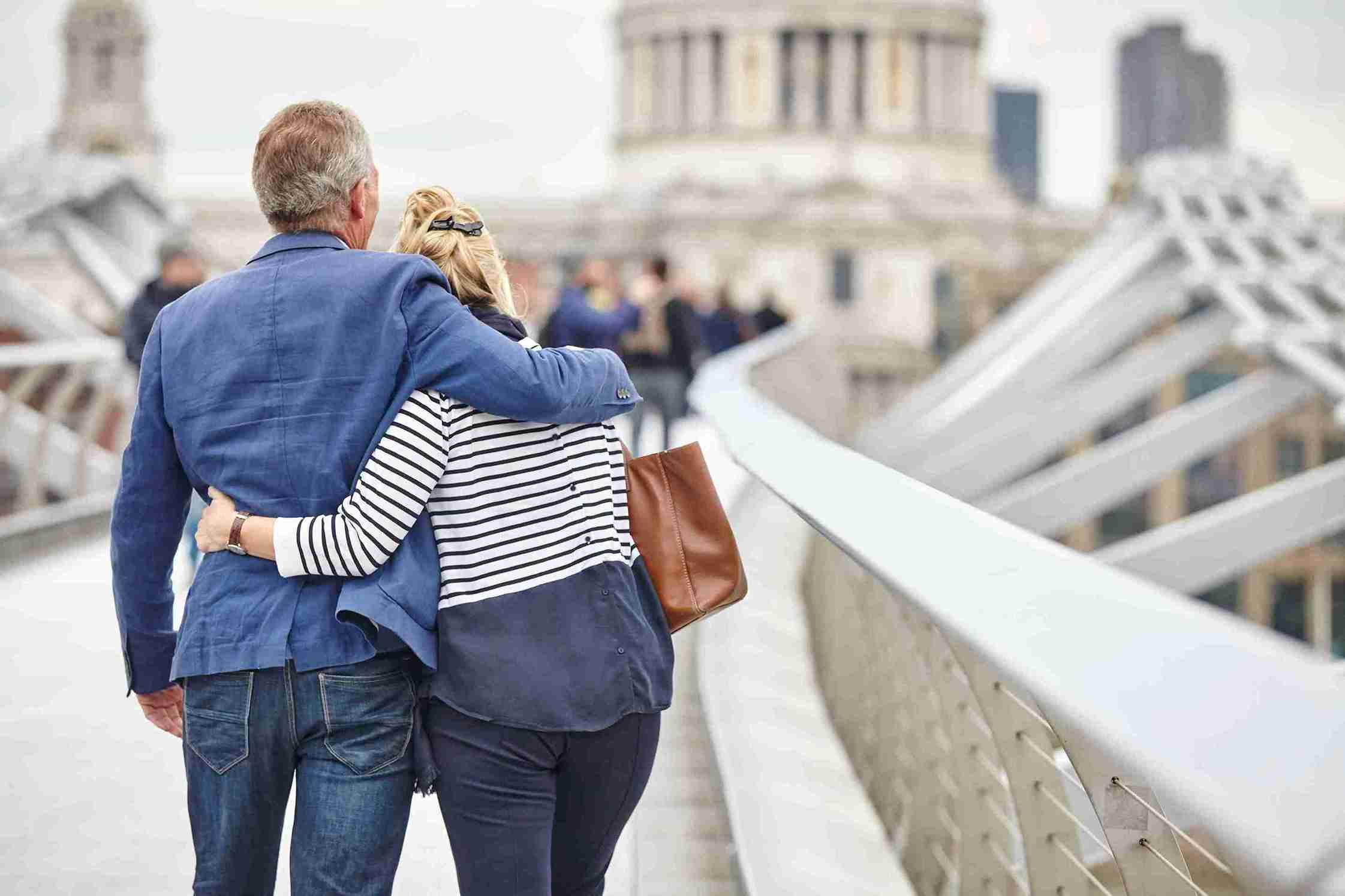 Rear view of mature dating couple crossing Millennium Bridge, London, UK