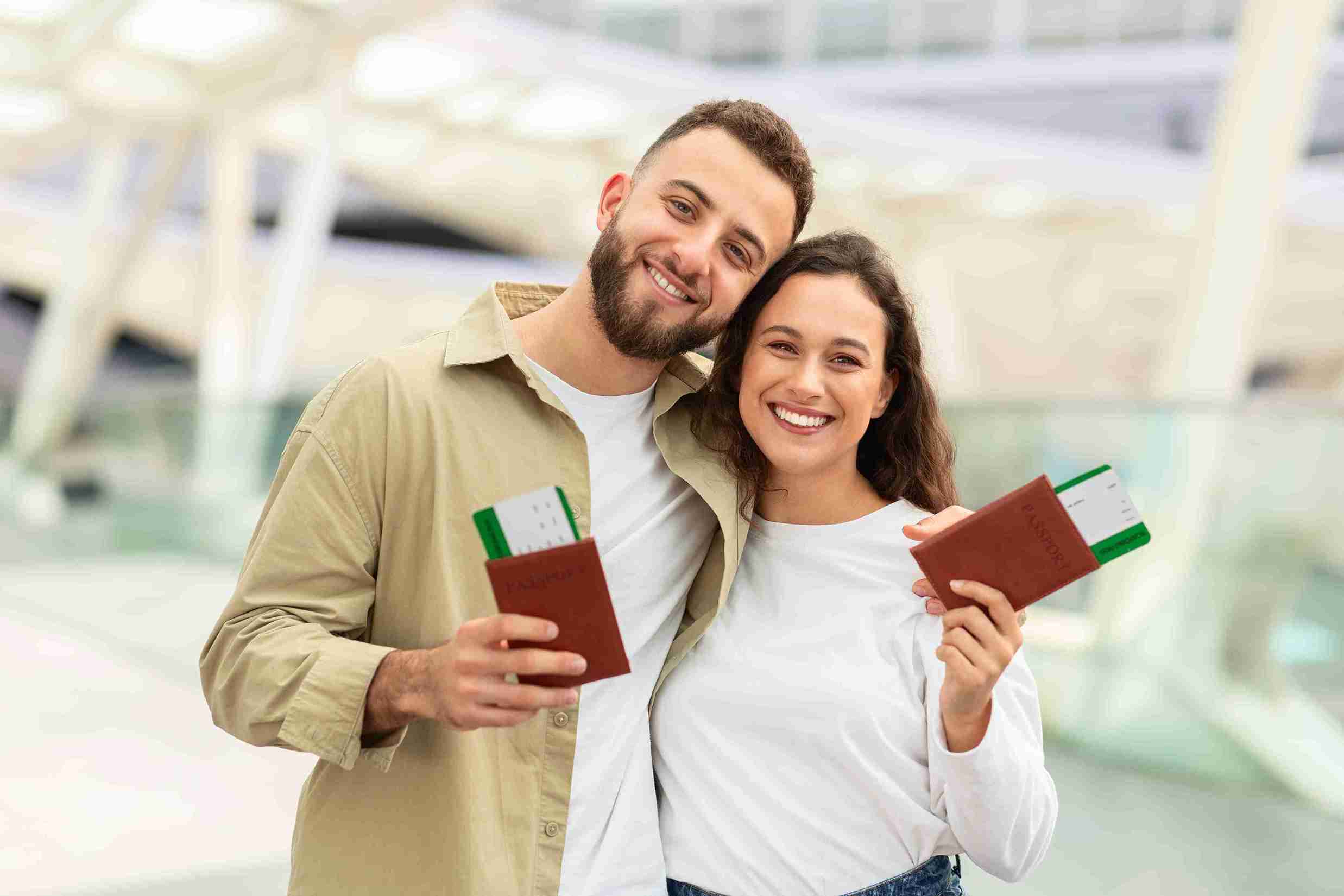 A man and woman proudly hold up their passports, smiling against a neutral background.